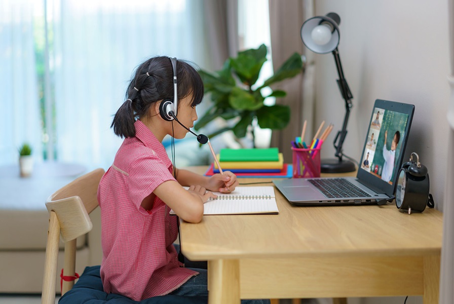 Fotografía de niña con audífonos, escribiendo mientras realiza sus tareas frente a un computador /fuente: Observatorio de Innovación Educativa